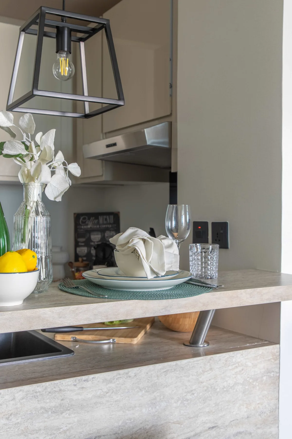 A kitchen counter is set with plates, glasses, and a folded napkin.