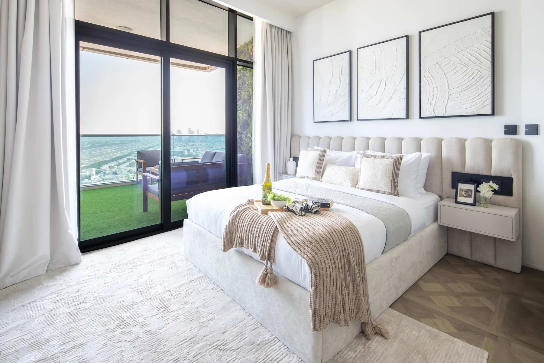 A bright bedroom with a neatly made bed beside large glass doors.