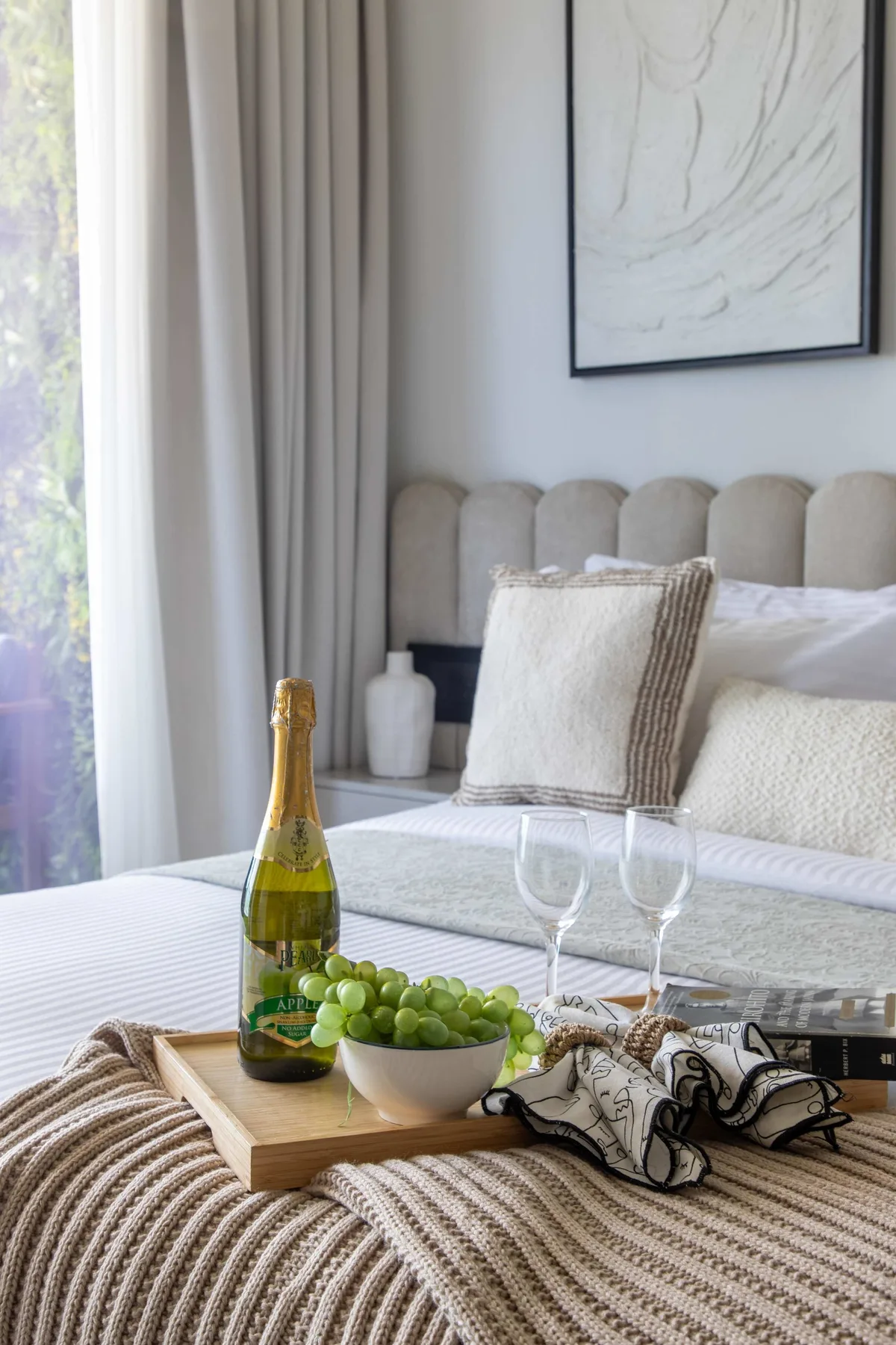 A bedroom with a bed, bedside table, and a tray of grapes and sparkling wine.