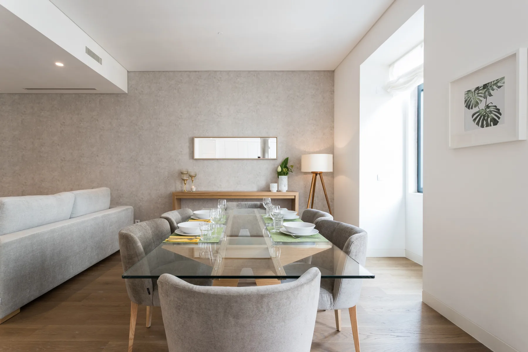 Una luminosa sala de estar y comedor tiene una mesa de cristal y asientos.