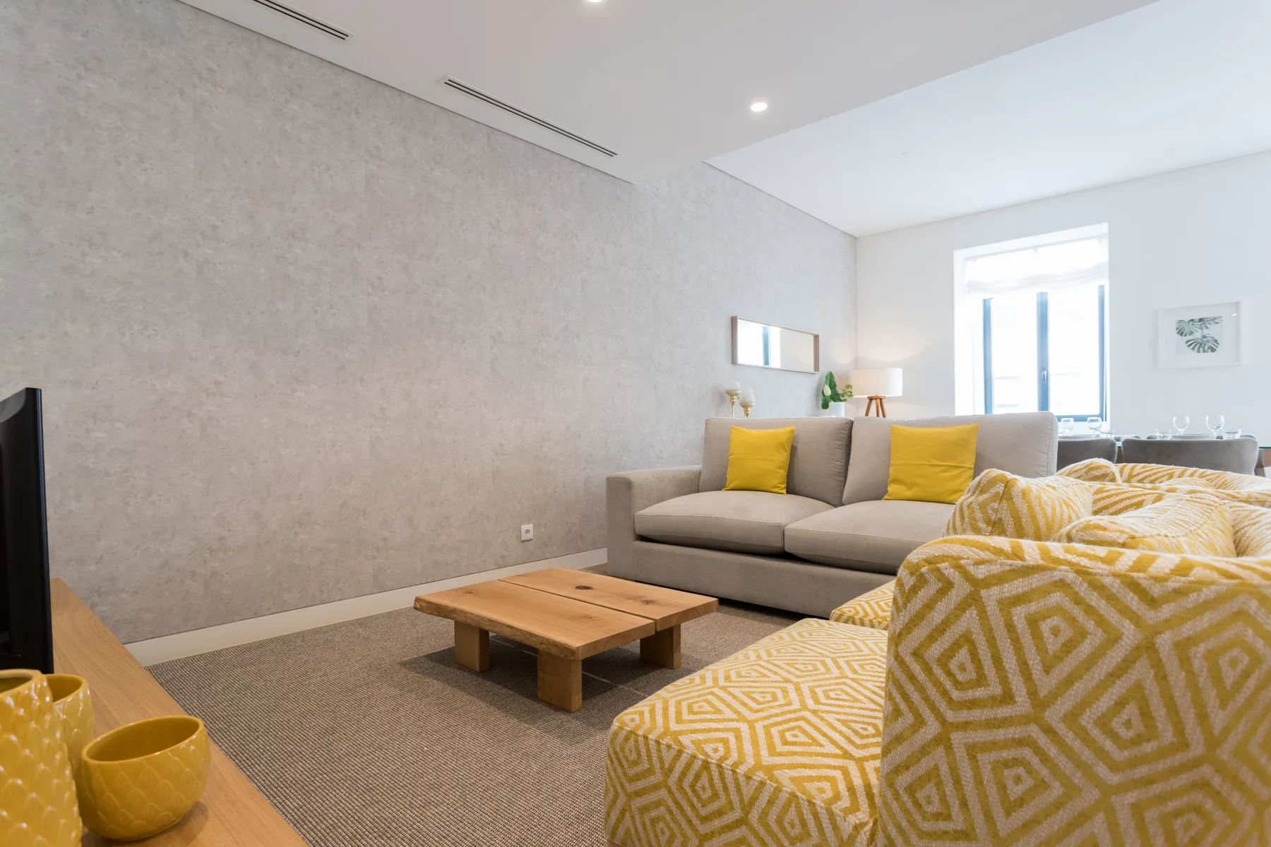 Una sala de estar con sofá gris, mesa de centro de madera y asientos amarillos estampados.