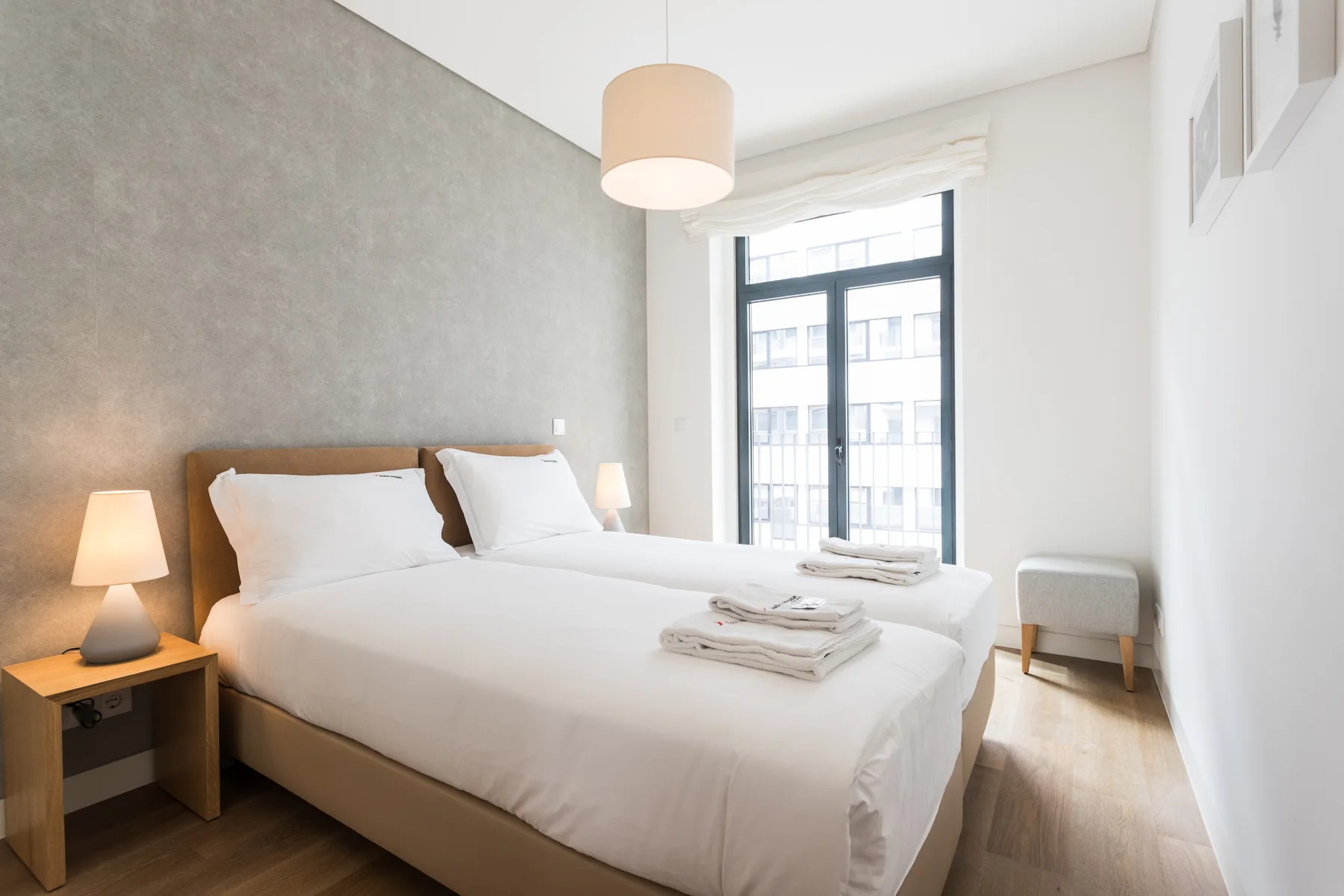 Un dormitorio luminoso con una cama bien hecha junto a una ventana grande.