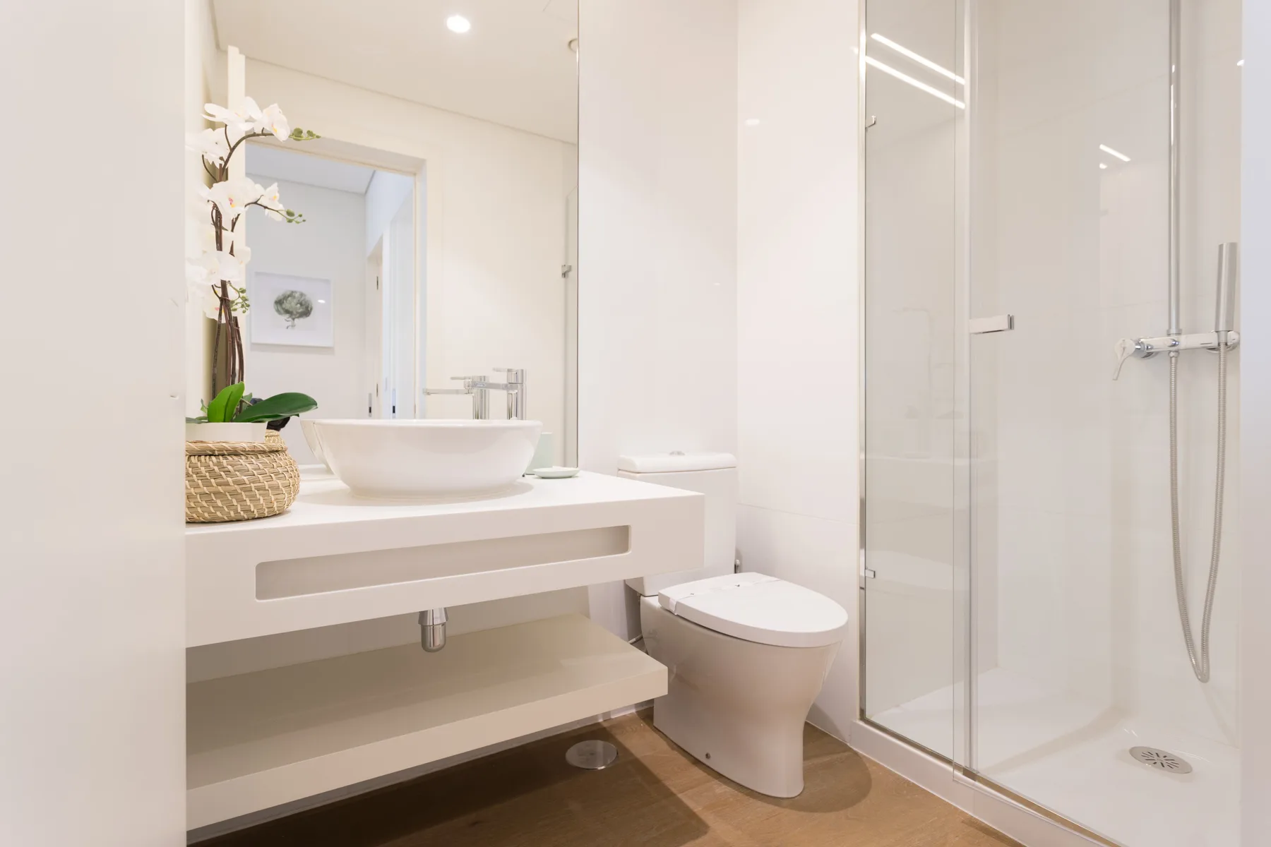 Un baño luminoso con lavabo blanco, inodoro y ducha de vidrio.