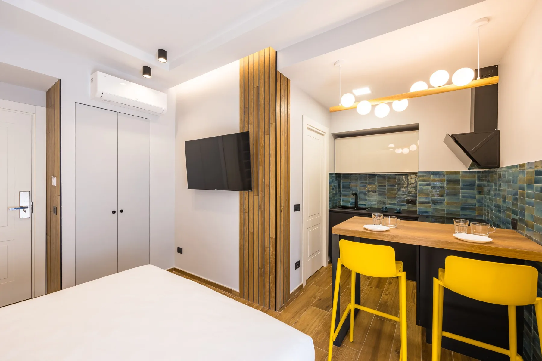 Un dormitorio luminoso se abre a una cocina compacta y una barra de comedor con asientos amarillos.