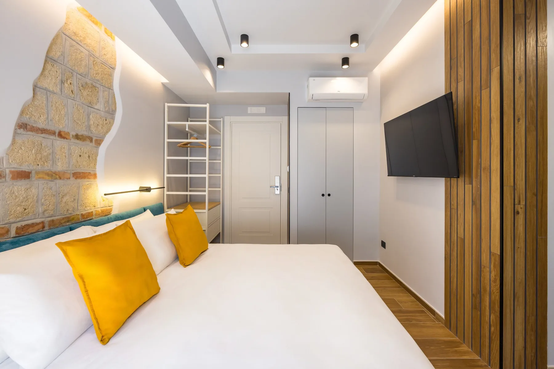 Un dormitorio con una cama blanca, almohadas amarillas y un televisor montado en la pared.