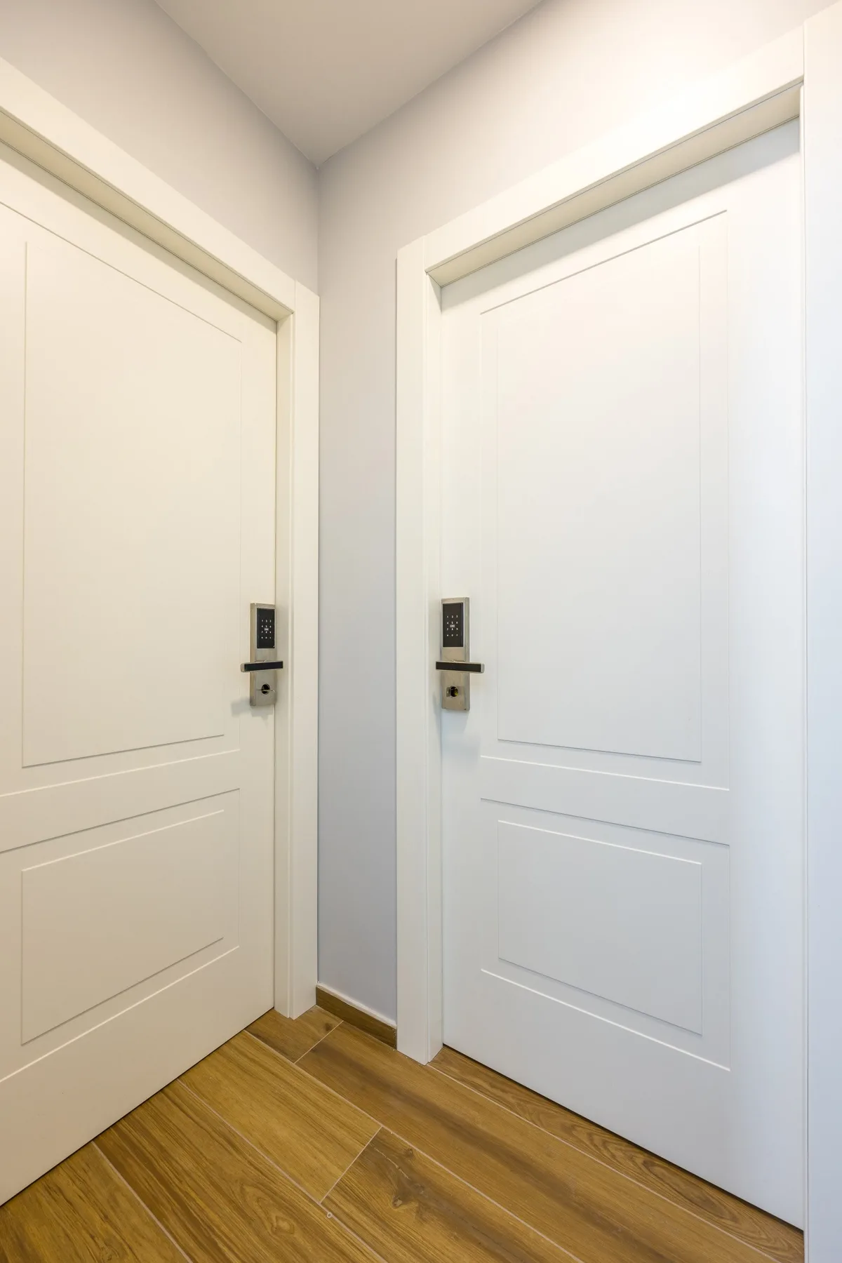 Un pasillo interior con dos puertas blancas y suelo de madera.