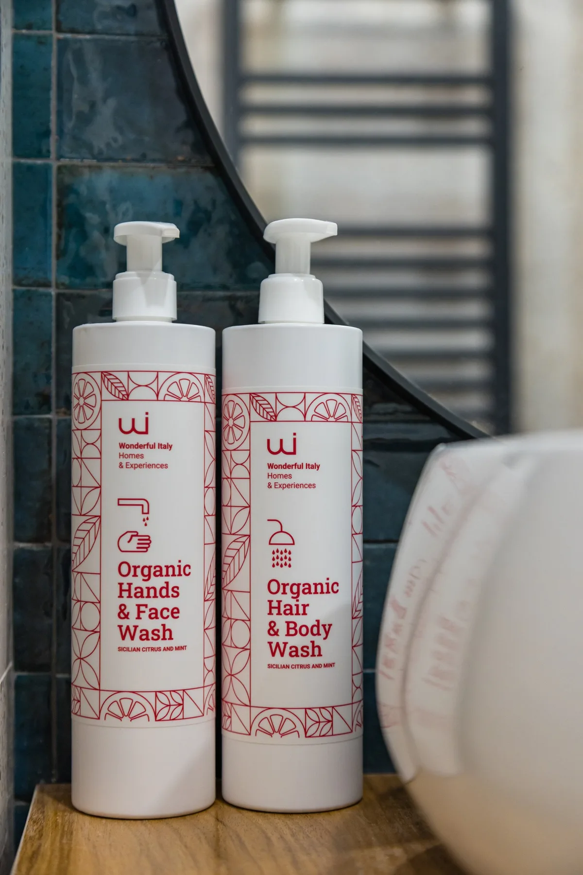Dos botellas con dispensador están sobre una encimera de baño junto a una pared de azulejos.