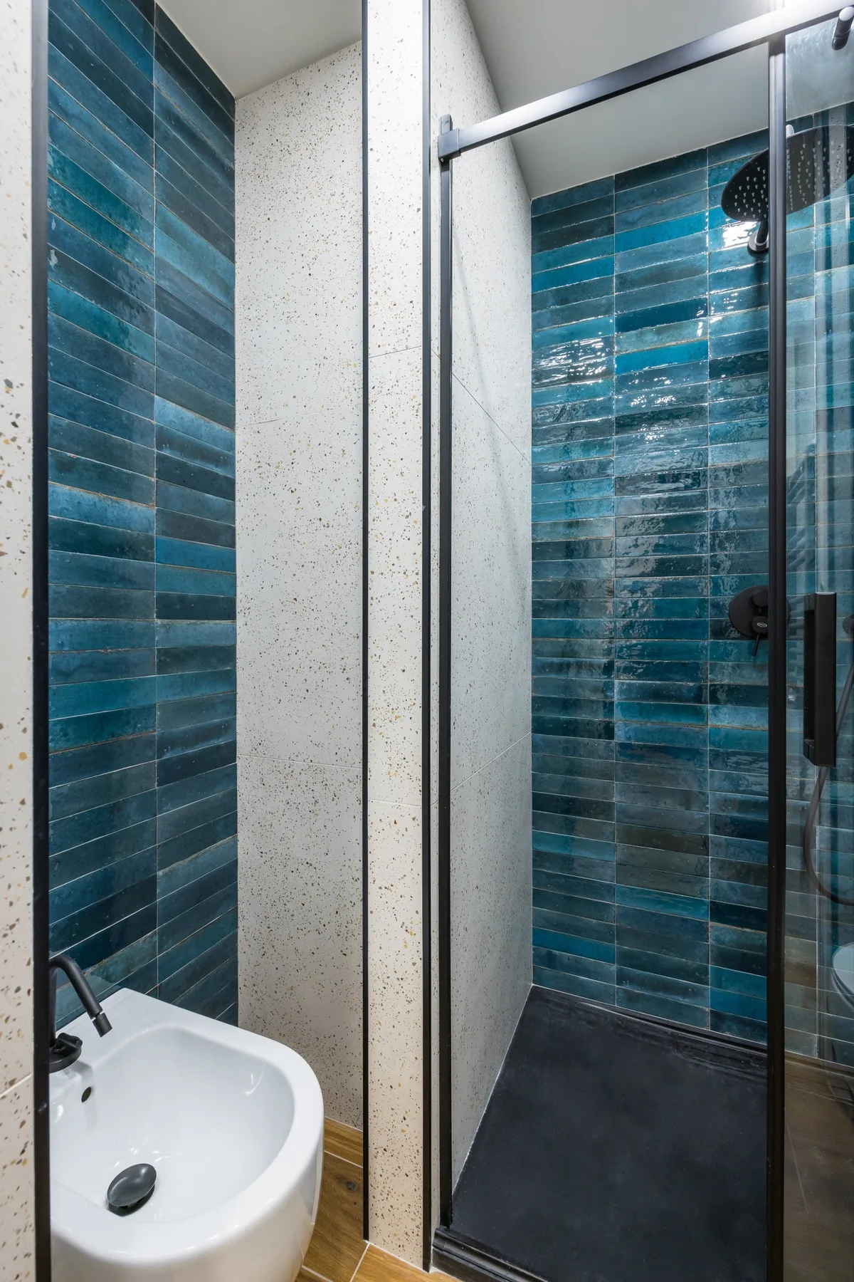 Un baño con una ducha de paredes de azulejos azules y un lavabo blanco.