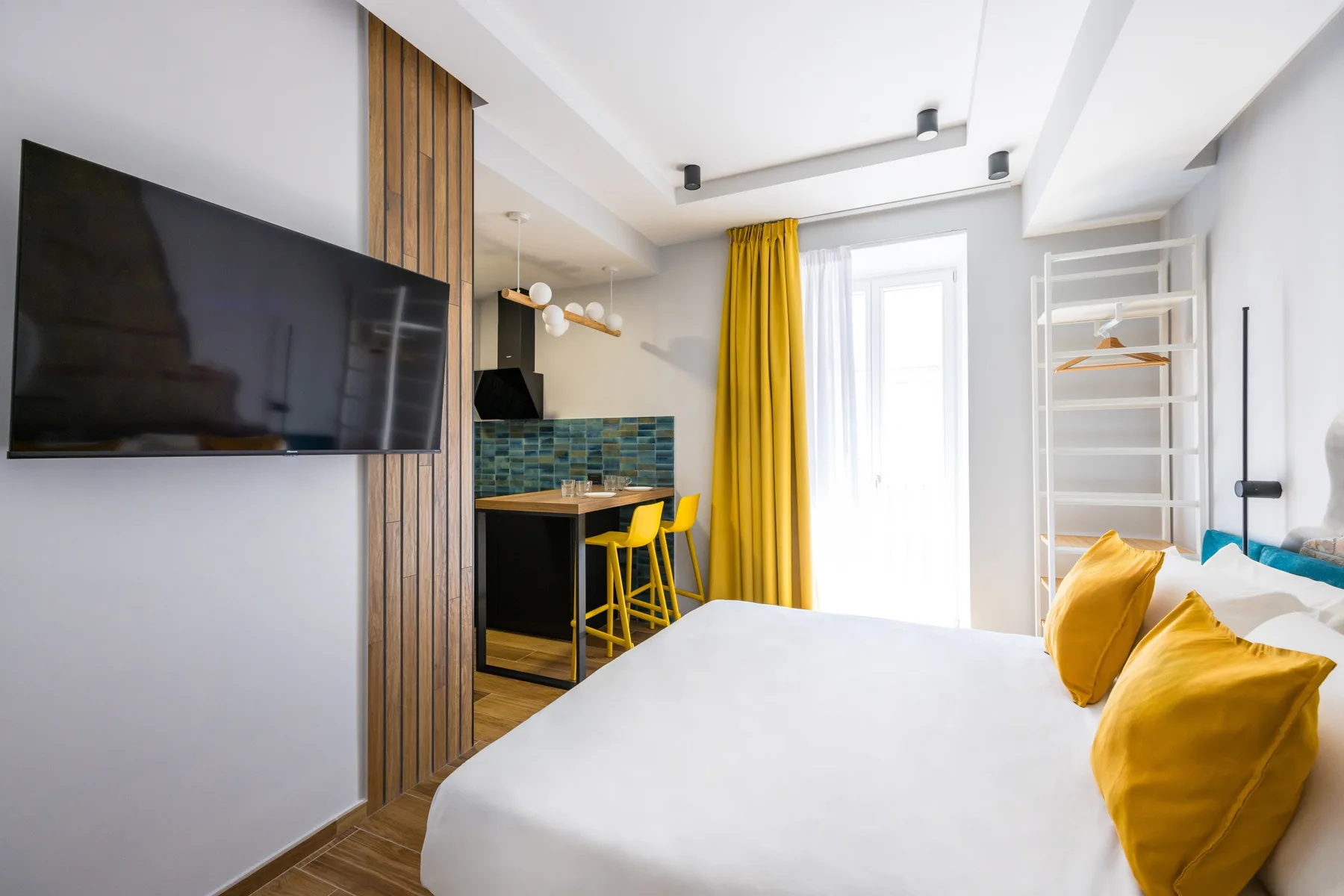 Un dormitorio luminoso con una cama blanca y una pequeña cocina.