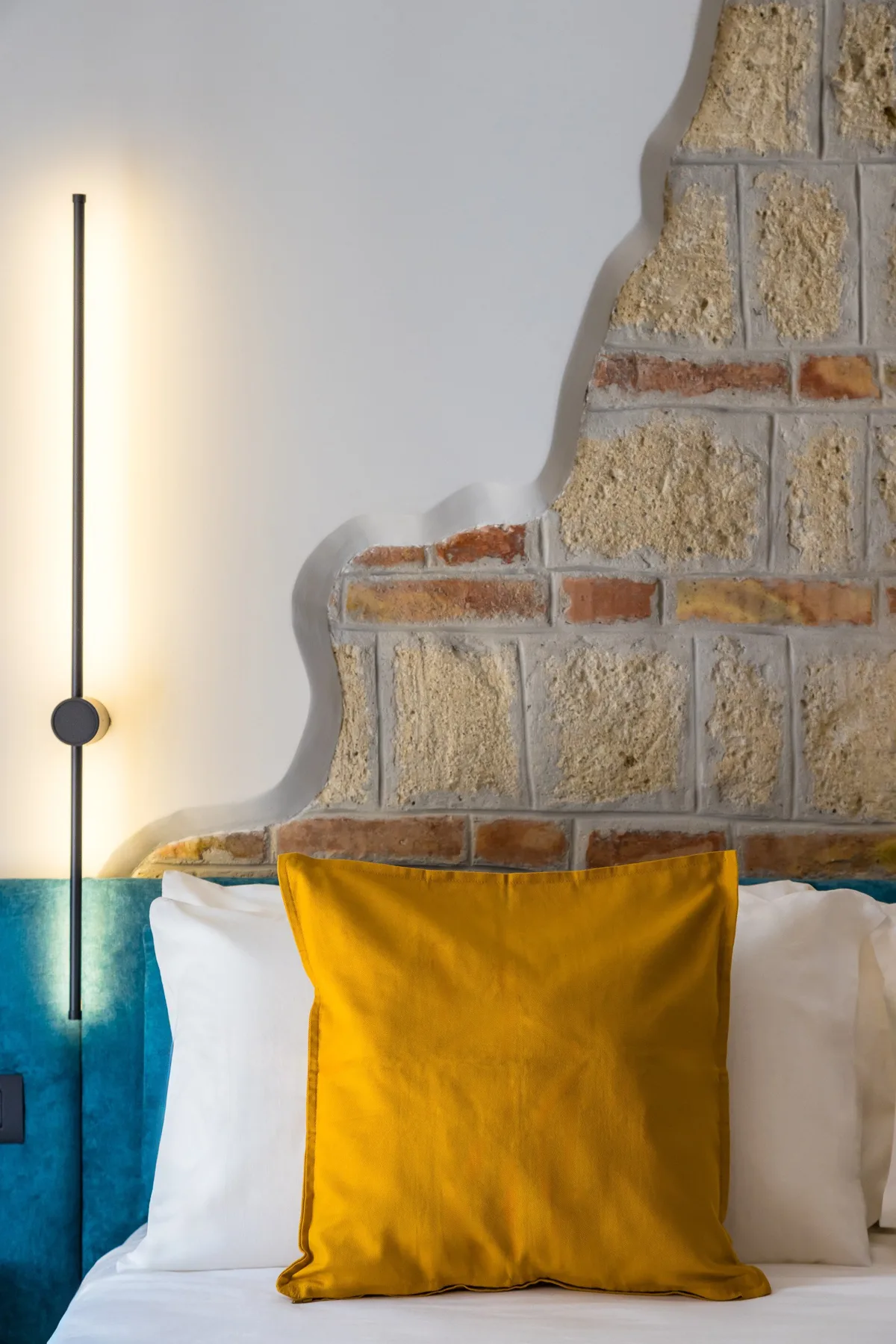 Una cama con un cojín mostaza está frente a una pared de piedra y ladrillo.