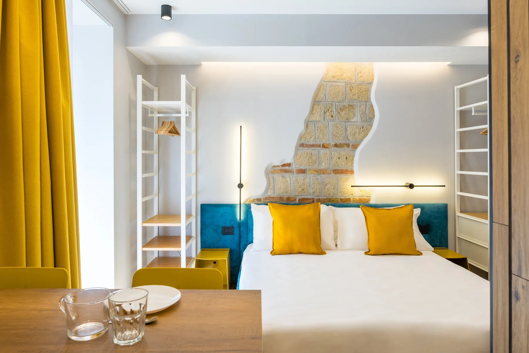 Un dormitorio con una cama, cortinas color mostaza y estanterías empotradas.