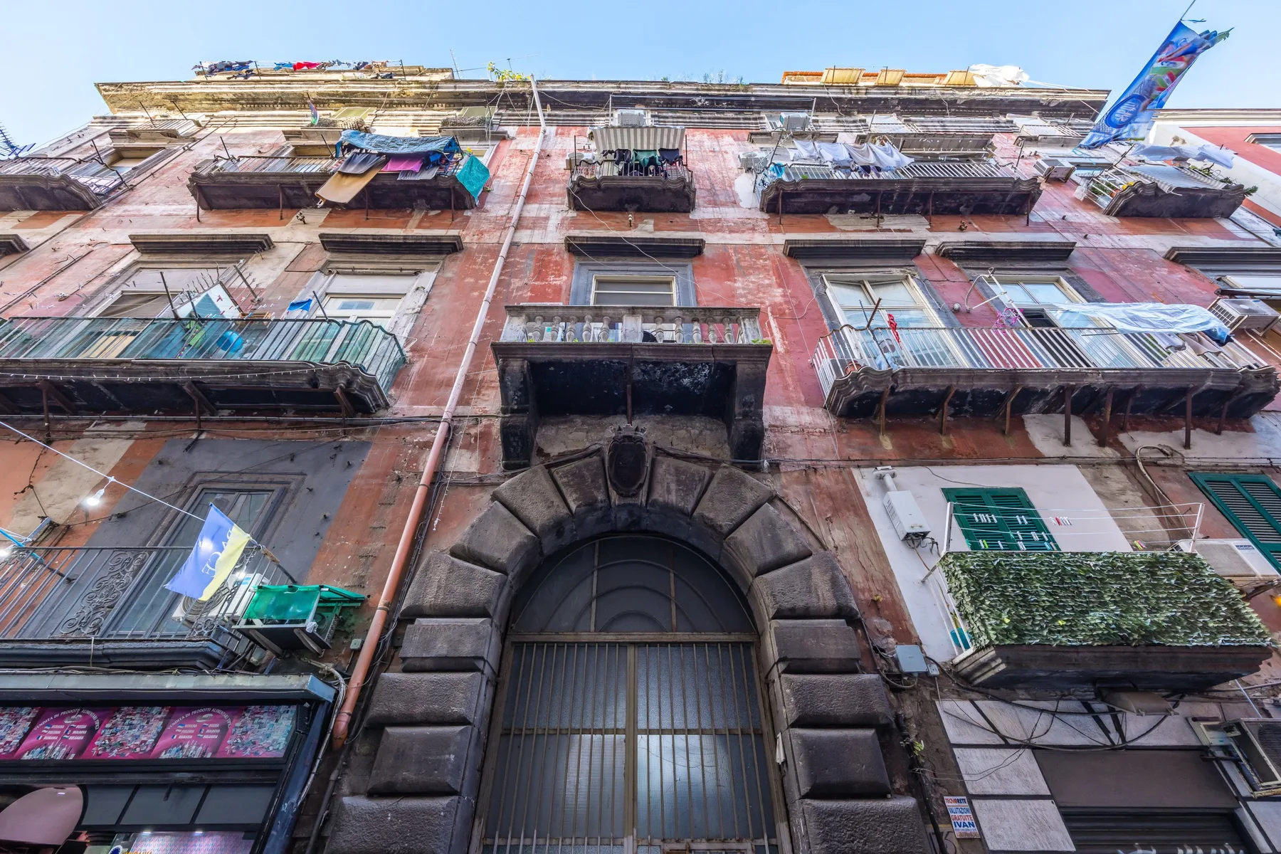 Vista desde abajo de una fachada de aspecto antiguo, con balcones y una gran entrada arqueada.