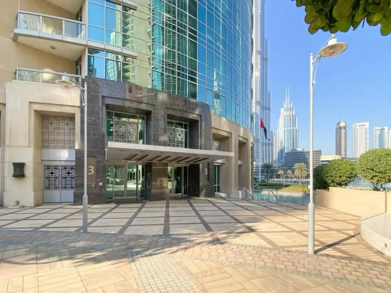 La entrada de un edificio moderno con fachada de vidrio da a una plaza pavimentada.