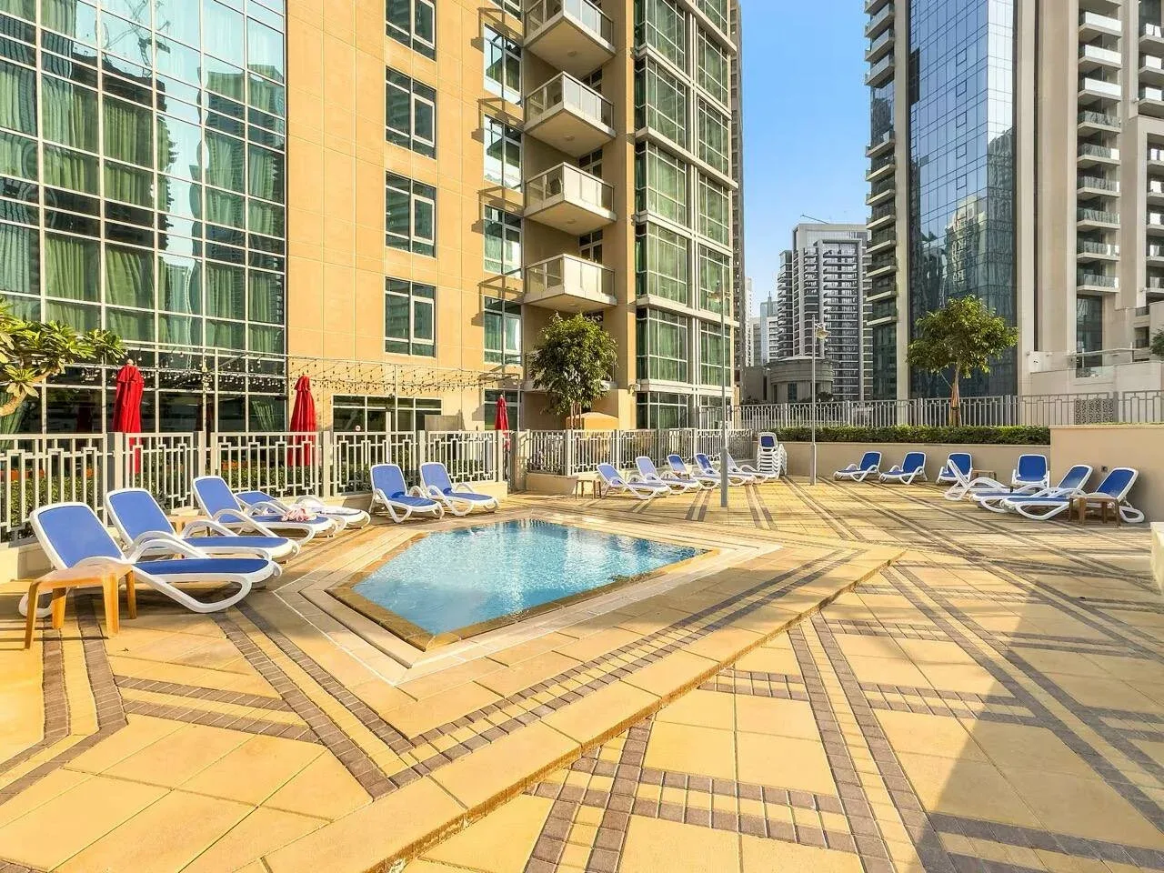 Una zona de piscina al aire libre con tumbonas y edificios altos al fondo.