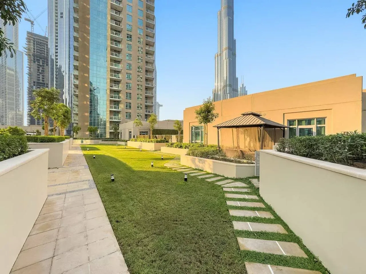 Un patio ajardinado tiene césped, senderos pavimentados y edificios altos alrededor.