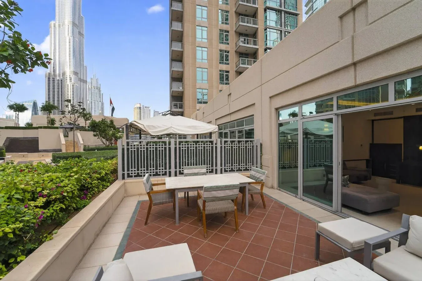Un patio al aire libre con mesa de comedor, asientos y una sombrilla junto a un edificio.