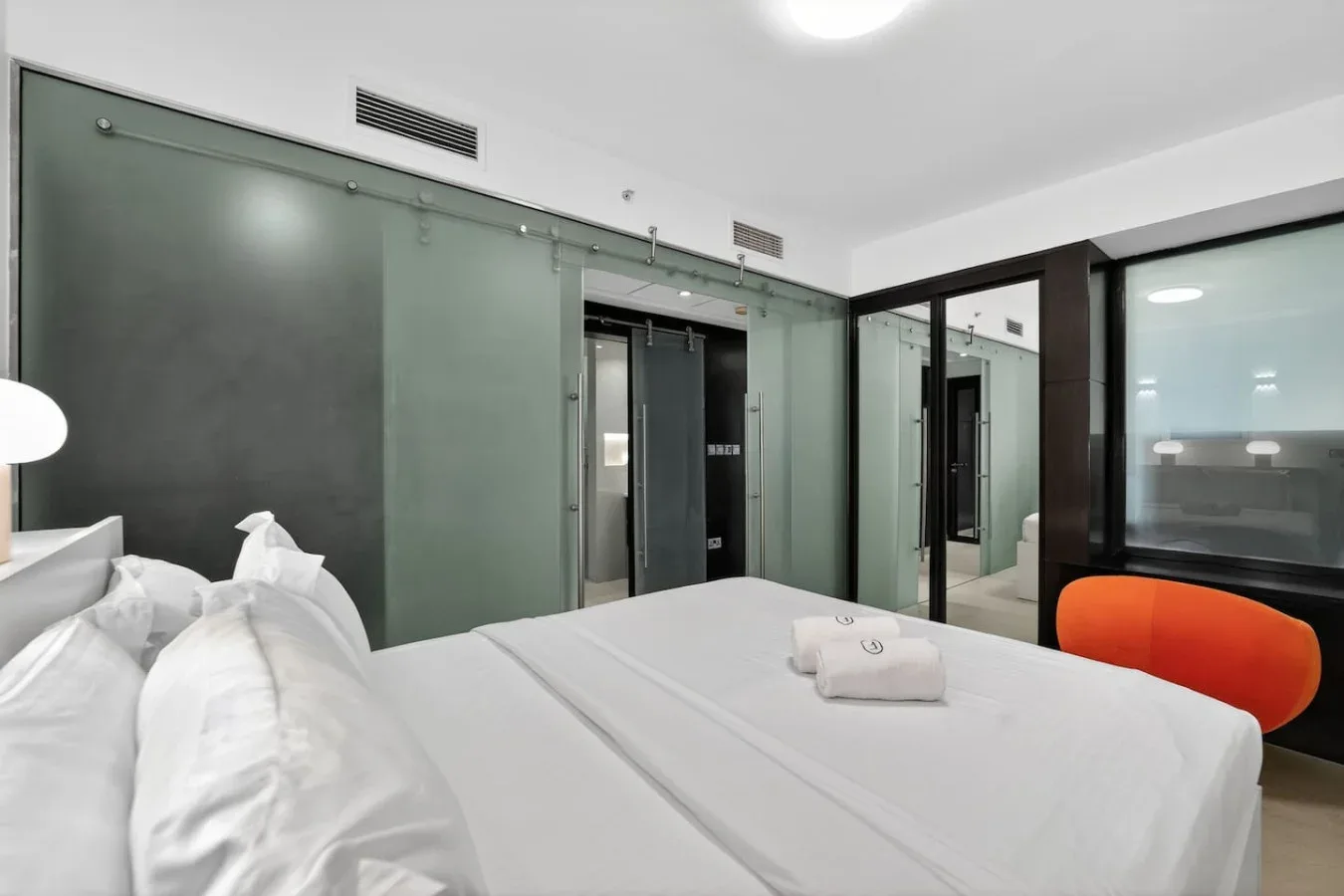 Un dormitorio con una cama bien tendida y separaciones de vidrio.