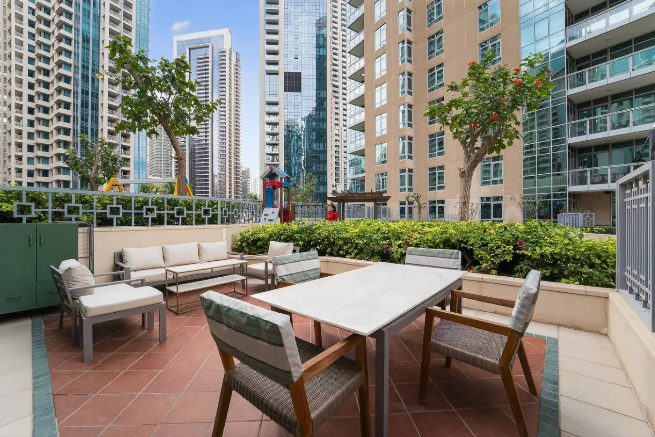 Un patio al aire libre tiene una mesa de comedor y asientos entre edificios altos.