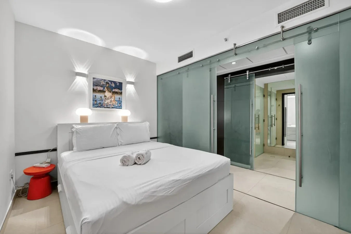 Un dormitorio con una cama blanca junto a una puerta corrediza de vidrio.