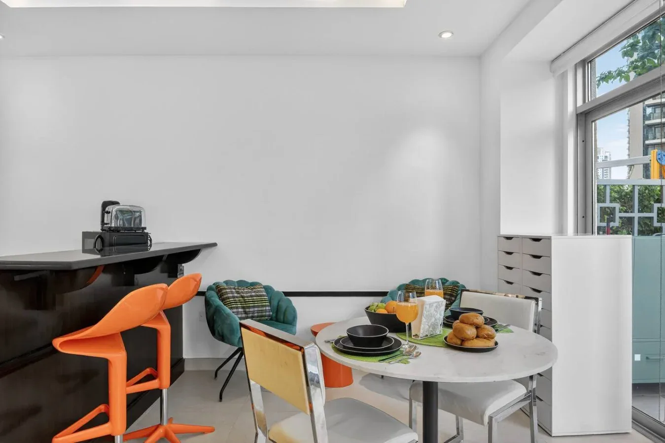 Un comedor luminoso tiene una mesa redonda con platos junto a una barra oscura.