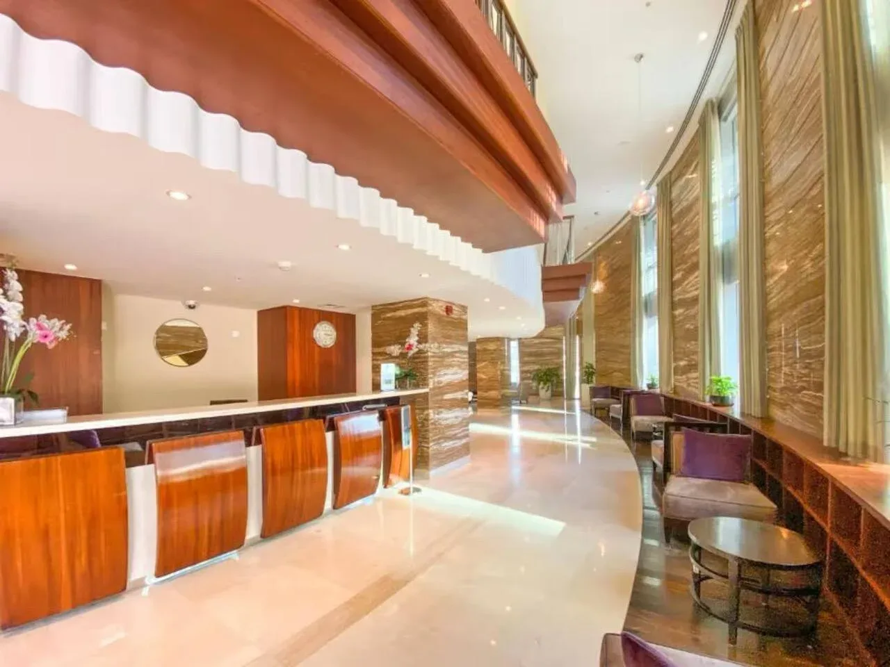 Una recepción de hotel con un mostrador largo de madera y asientos junto a las ventanas.