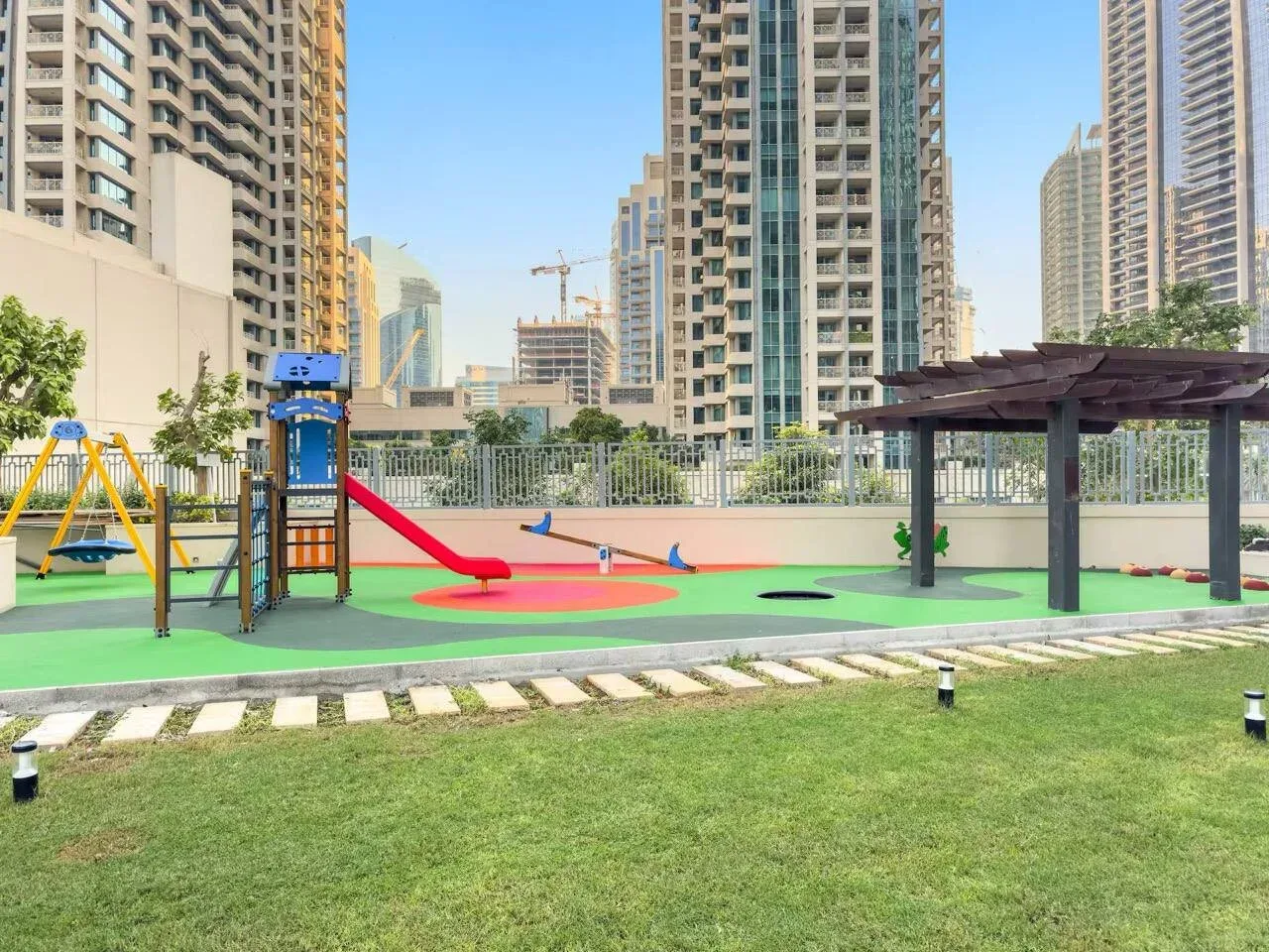 Un parque infantil al aire libre con juegos coloridos está rodeado de edificios residenciales altos.