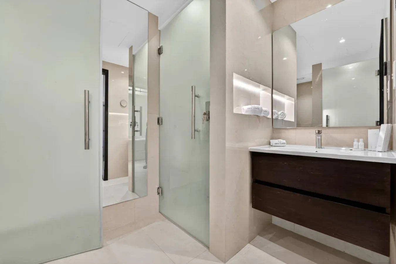 Un baño moderno con ducha de vidrio y un lavabo suspendido bajo un espejo grande.