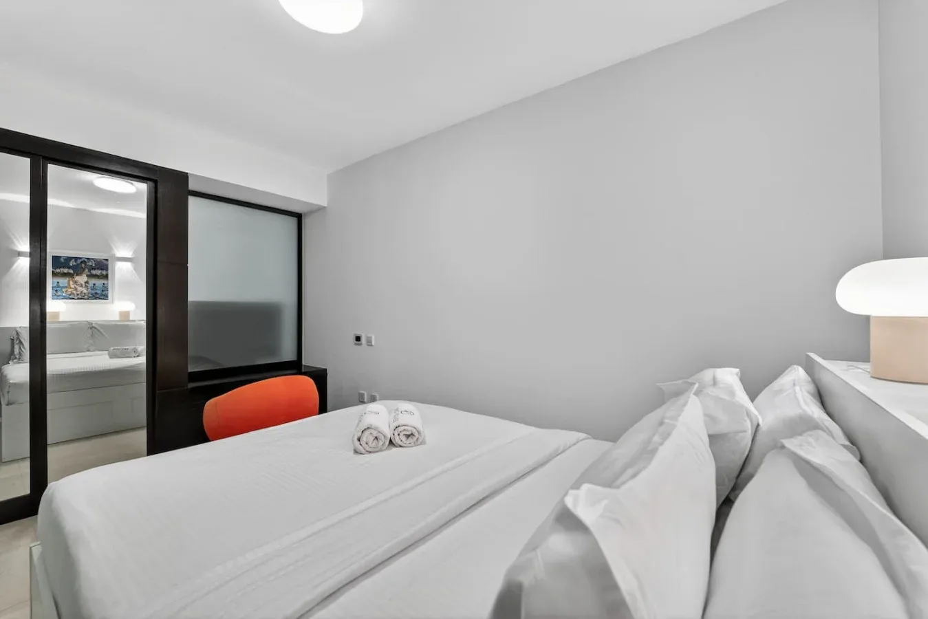 Un dormitorio con una cama bien tendida y una mampara de vidrio hacia el baño.