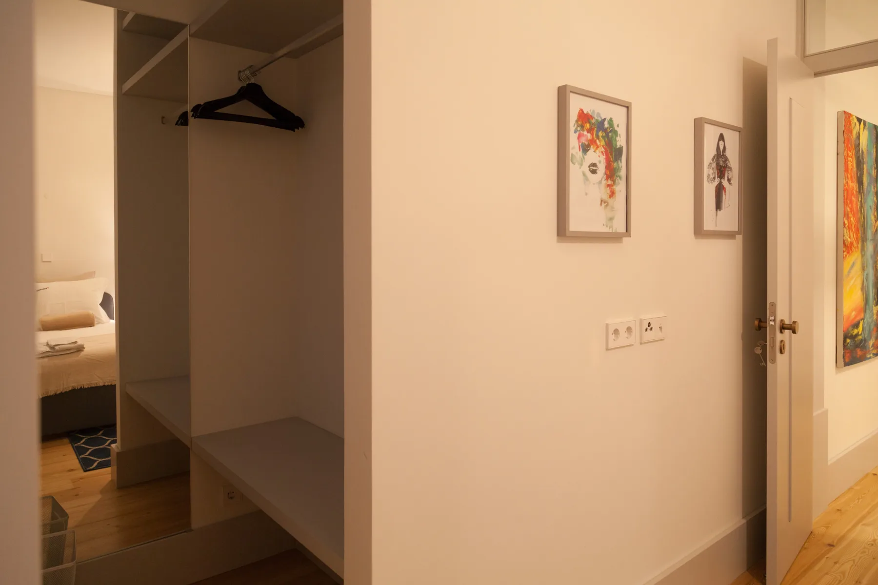 A hallway with an open closet and framed artwork on the walls.