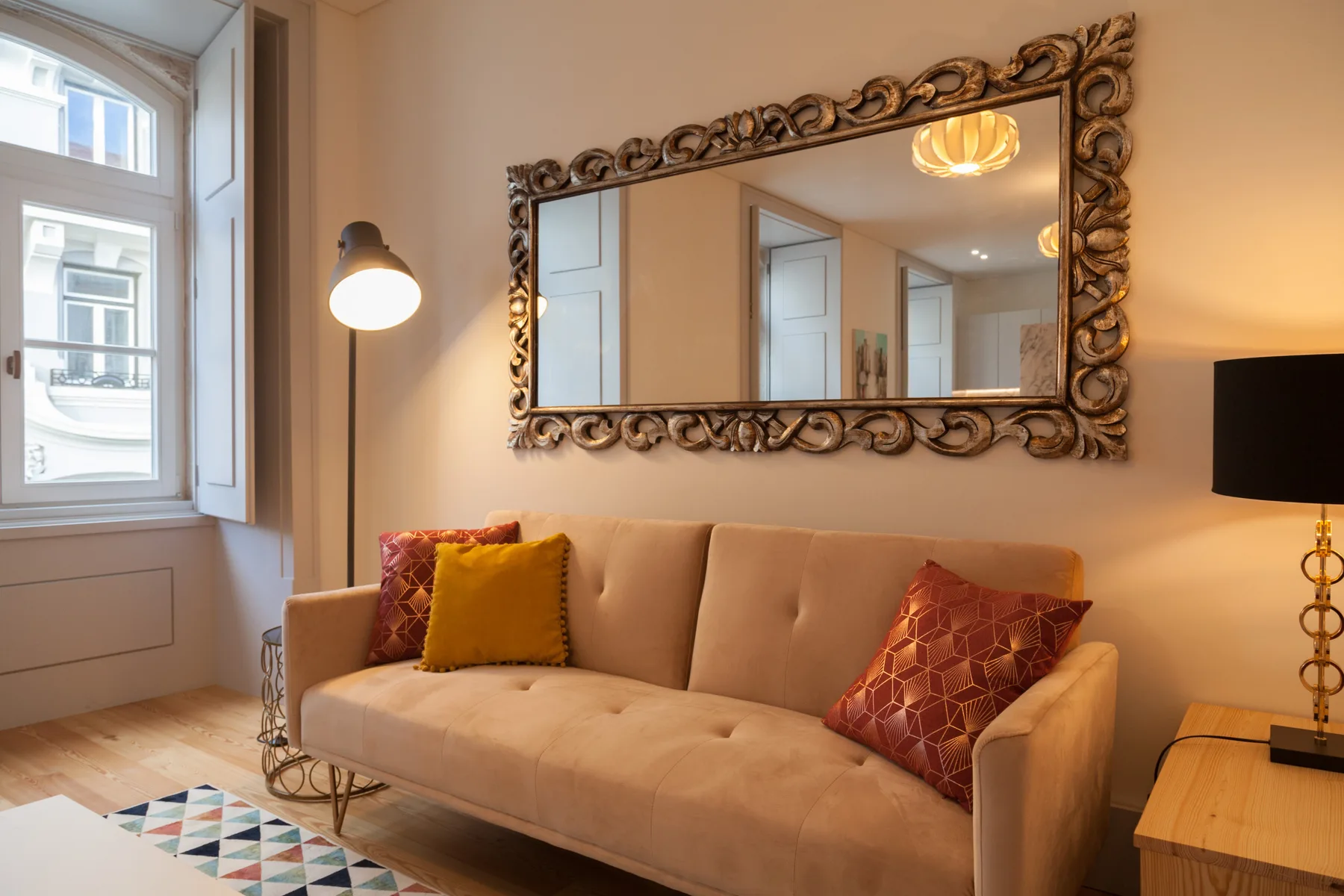 A living room with a beige sofa, colorful cushions, and an ornate wall mirror.