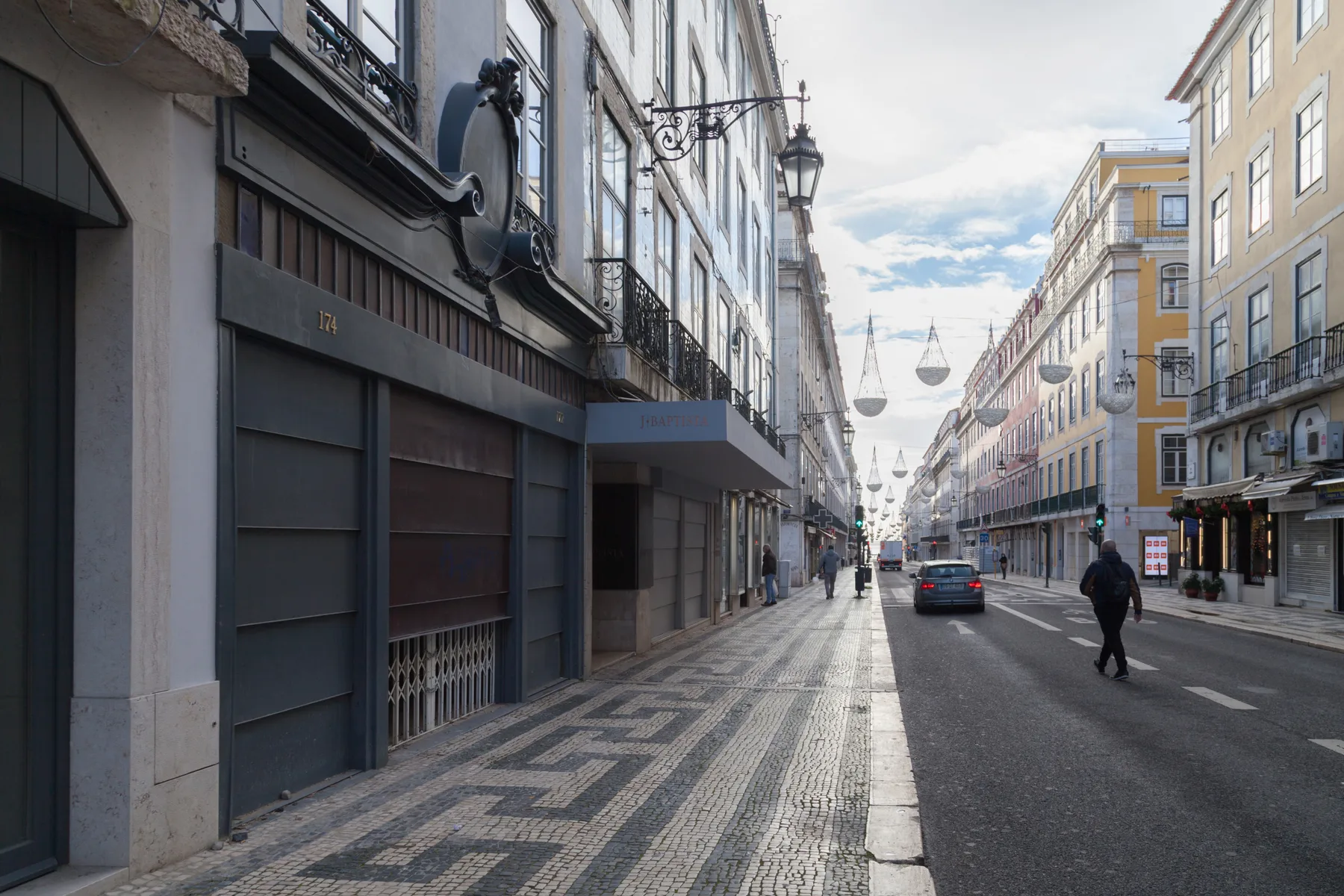 A city street with tall buildings, patterned sidewalks, and decorative lights overhead.