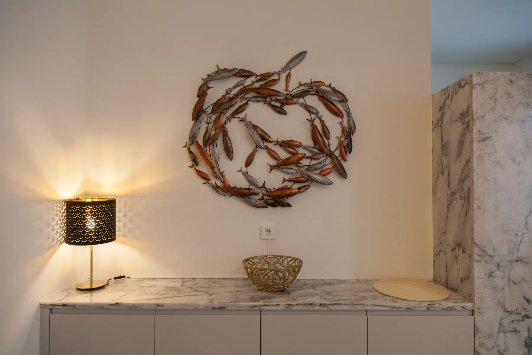 An interior console is topped with a decorative metal fish sculpture and a lit lamp.