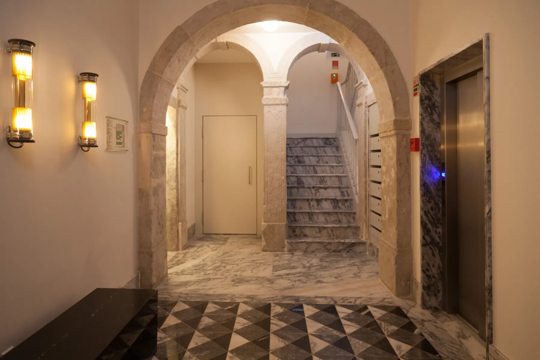 An arched interior hallway with a staircase and an elevator.