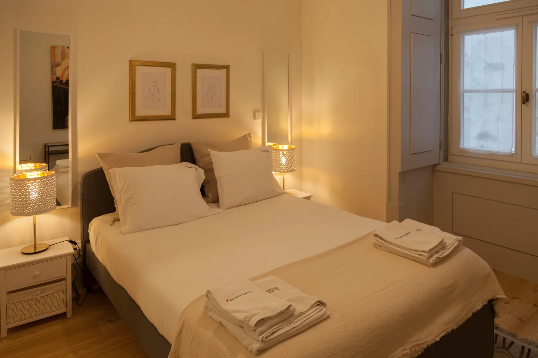 A bedroom with a neatly made bed, bedside tables, and framed wall art.