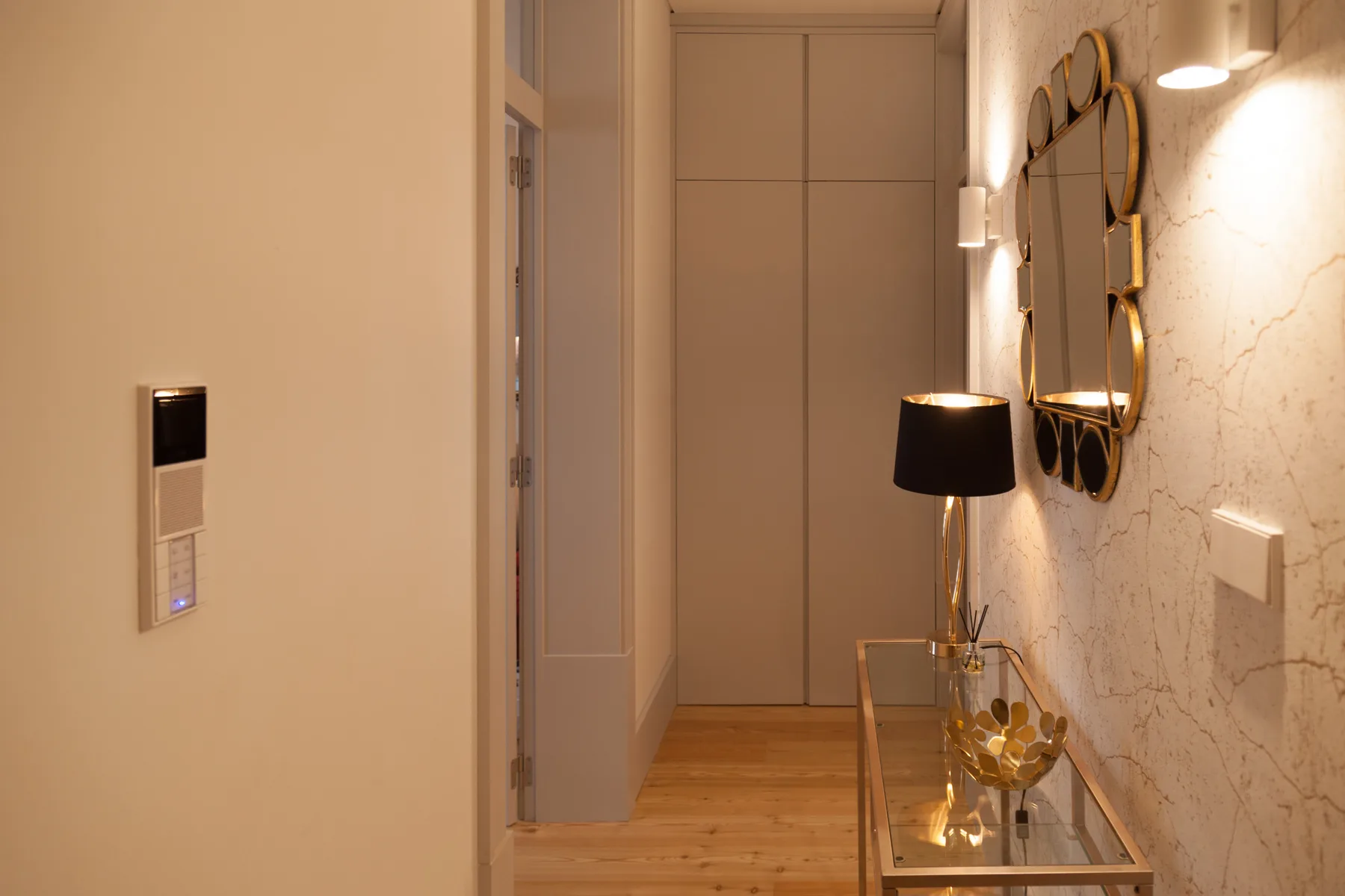 A warm-lit hallway with a narrow glass console table and decorative wall mirrors.