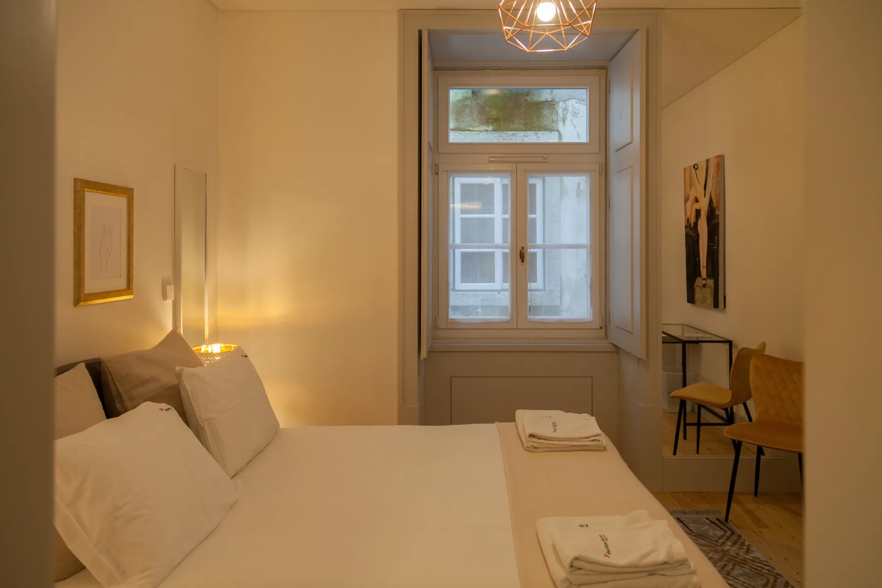 A bedroom with a neatly made bed and a window at the far end.
