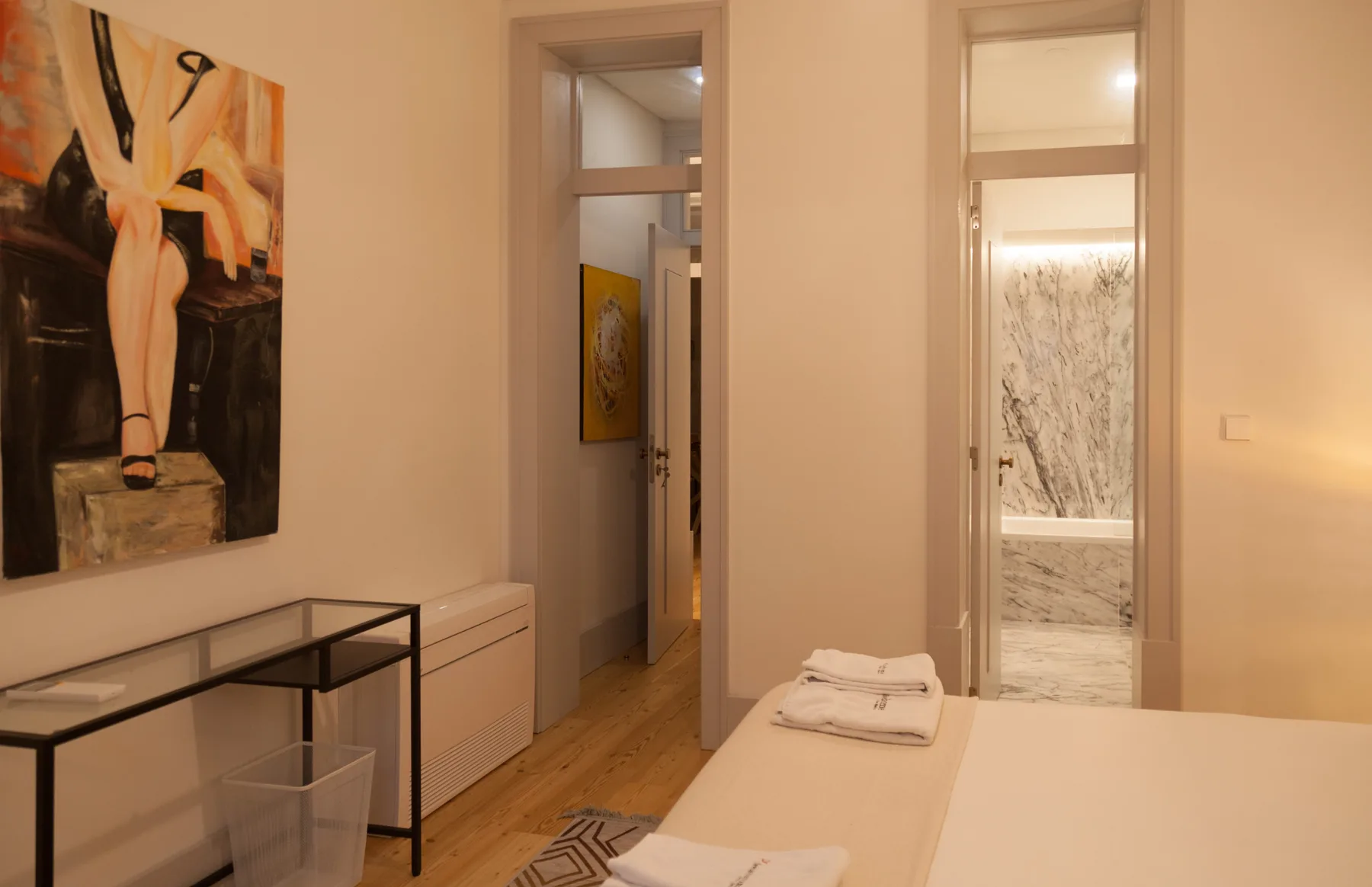 A bedroom with a bed, folded towels, and a large painting on the wall.