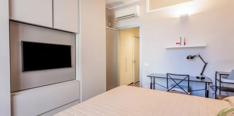 Un dormitorio con cama, televisor en la pared y una pequeña zona de escritorio.