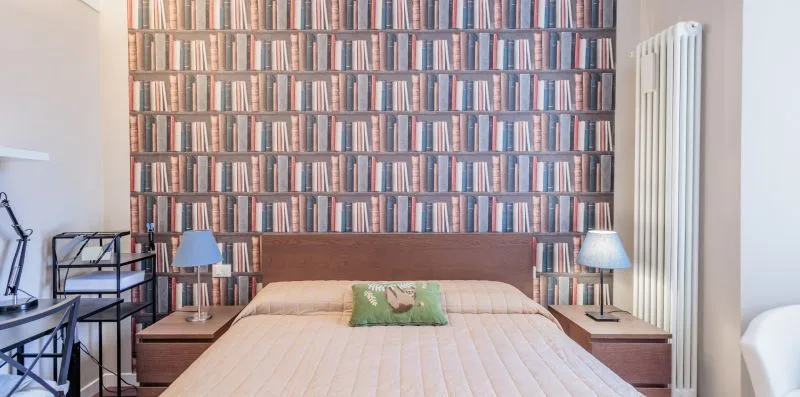 Un dormitorio con una cama bien tendida y una pared cubierta de libros.