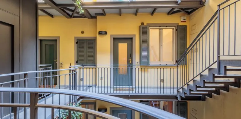 Un pasillo de patio interior con barandillas metálicas y una escalera.
