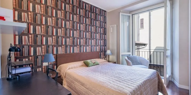 A bedroom with a double bed beside a wall of books and a glass balcony door.