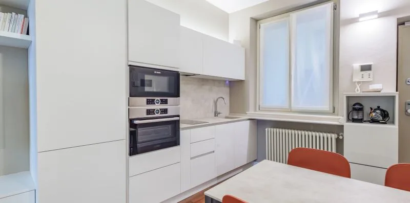 Una cocina luminosa con gabinetes blancos, electrodomésticos empotrados y una mesa de comedor.