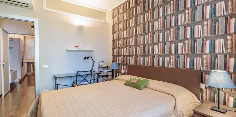 Un dormitorio con una cama y una pared cubierta de papel tapiz con motivos de libros.