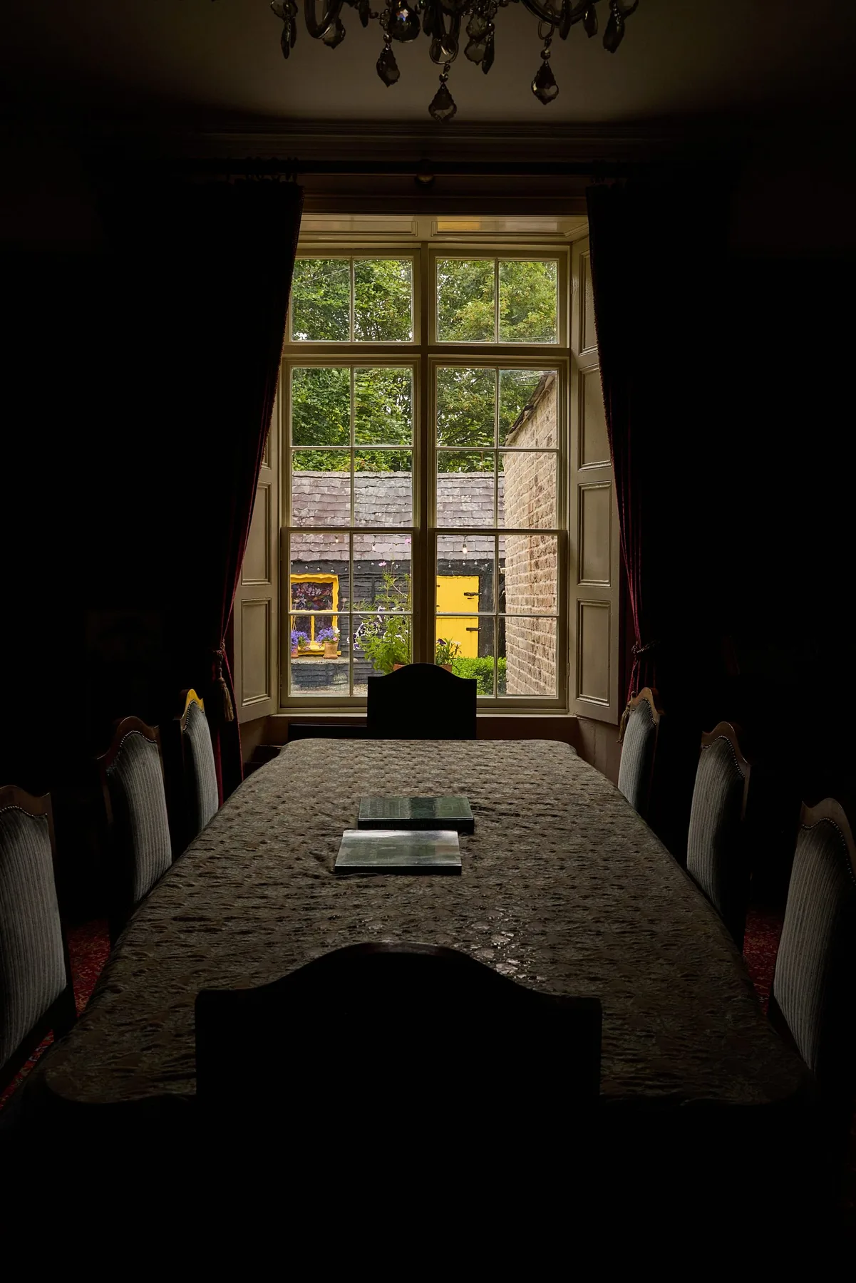 Dining room with a long table and chairs beside a large window.