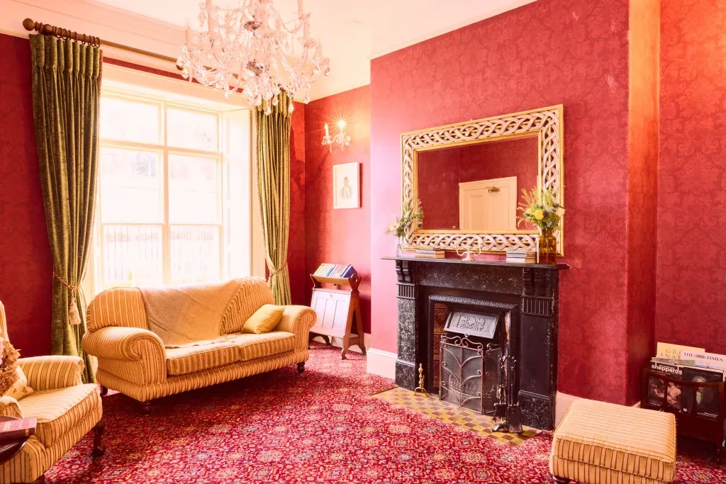 Living room with patterned wallpaper and carpet, sofas, fireplace and chandelier.