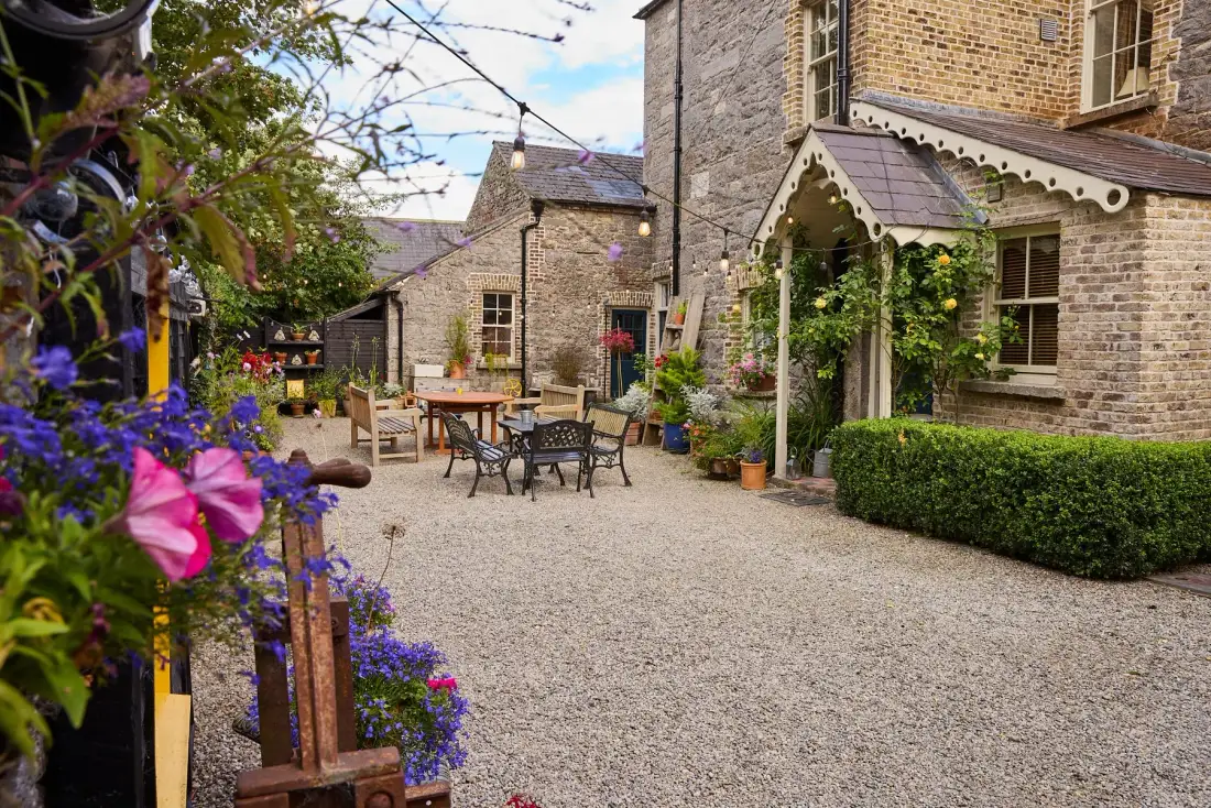 Gravel courtyard with outdoor tables and chairs, greenery and string lights.