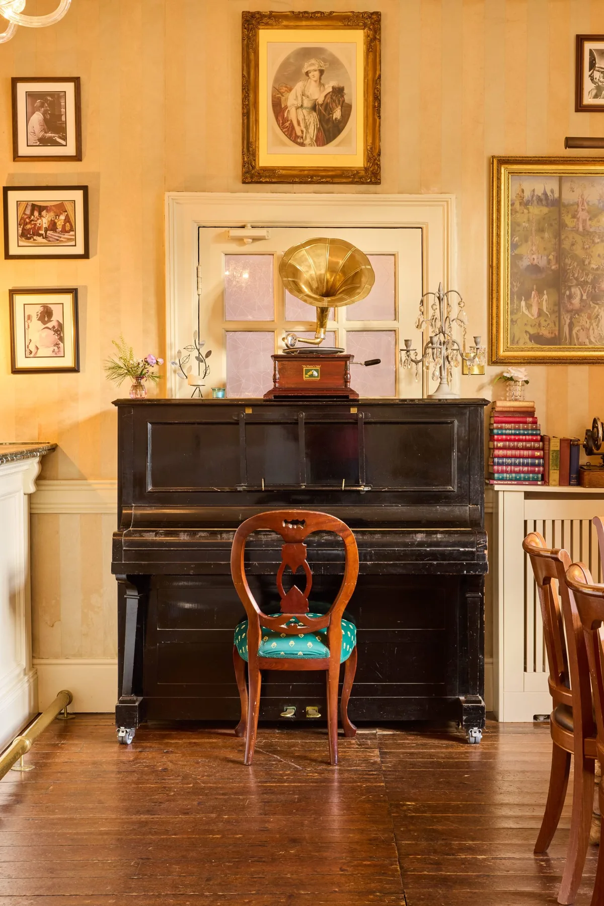 Vintage room with a piano, gramophone, ornate chair, artwork and books.