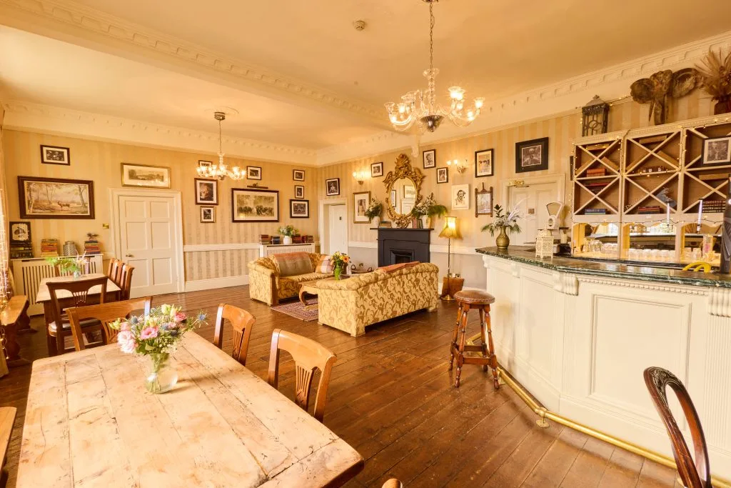 Vintage-style lounge with wooden floors, chandeliers, sofas and a bar.