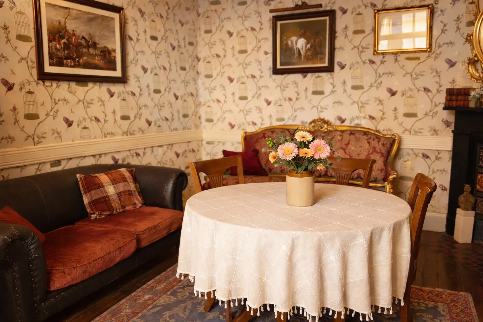 Reception room with floral wallpaper, upholstered seating and framed paintings.