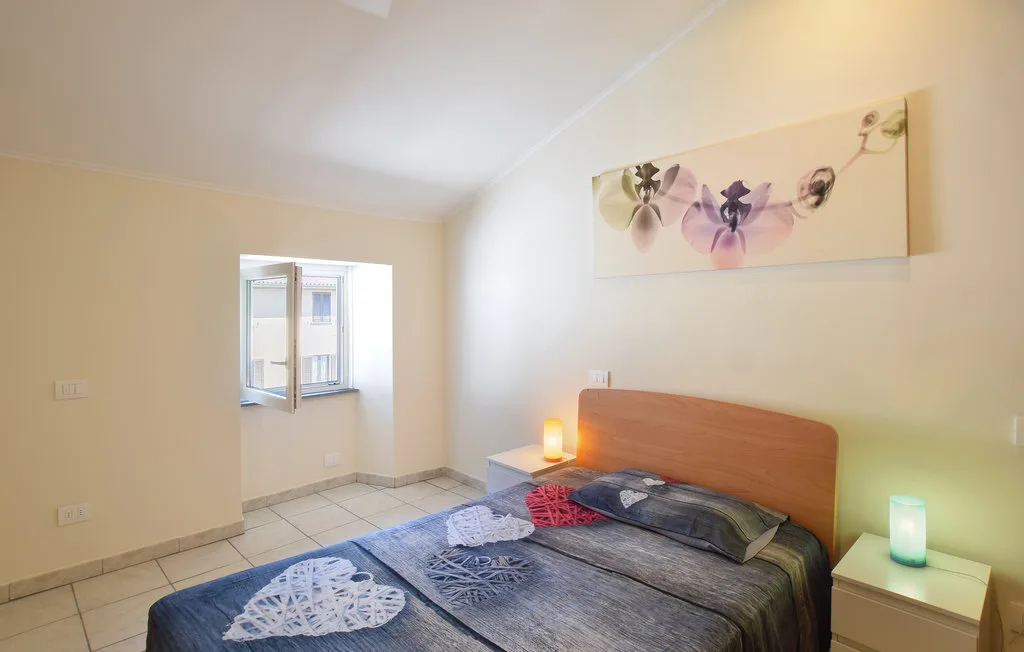 A bedroom with a bed beneath floral wall art and an open window.